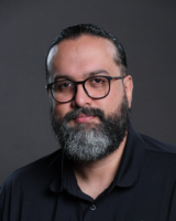 Professional photo of Fred Madrigal, wearing a black polo shirt against a dark background.