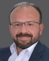 Headshot of Haitham Zaki in a navy blazer and white shirt, smiling with a gray background.